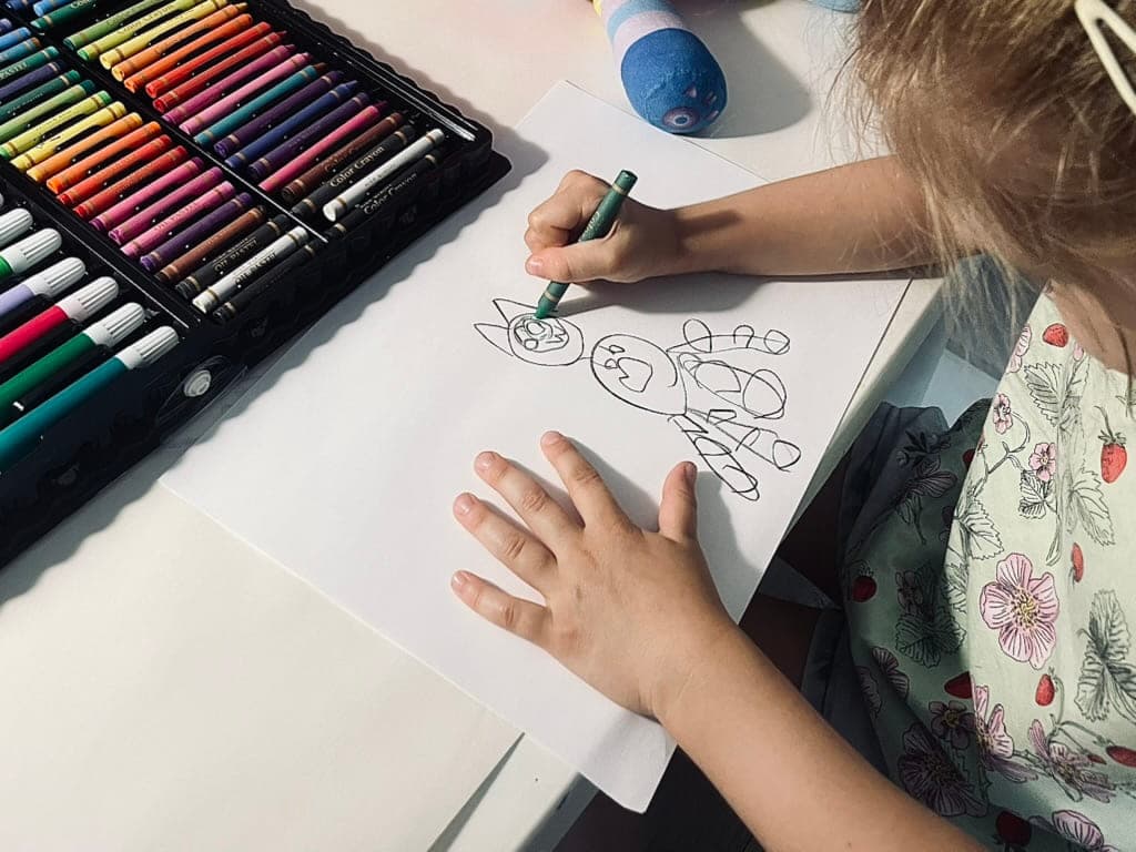 Dziecko rysuje flamastrem przy otwartym zestawie kredek
